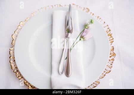 Ricevimento con tavolo per cena per matrimoni. Piatto bianco sopra un carattere jolly con bordi dorati. In un piatto bianco c'è un tovagliolo, un coltello, una forchetta e un viola Foto Stock