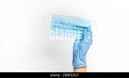 Mano con guanto di gomma protettiva per maschera chirurgica facciale bianca. Apparecchiature di protezione necessarie per l'uso durante la pandemia del virus della corona 2020. Foto Stock