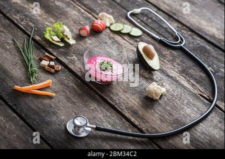 Faccia sorridente formata da verdure fresche crude, barbabietole, avocado dimezzato e stetoscopio in un'immagine concettuale di sano stile di vita e dieta. Foto Stock