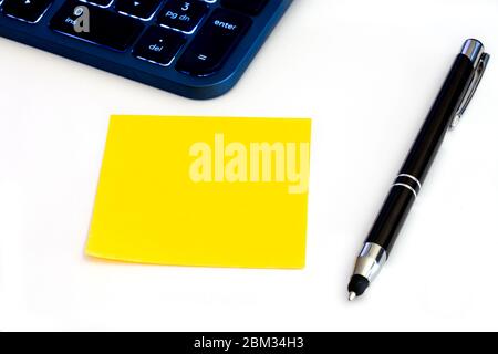 Promemoria giallo vuoto. Inserire la nota con la tastiera e la penna illuminate su un tavolo bianco Foto Stock