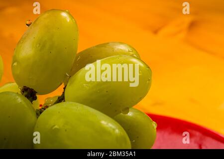 grande spazzola di uva verde in un piatto di ceramica rossa su sfondo ligneo Foto Stock