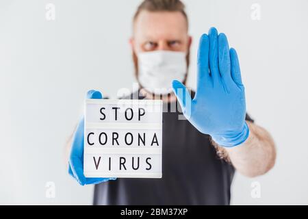 Stop Coronavirus Concept. Scatola luminosa con messaggio di testo Stop Coronavirus in mano all'uomo indossando guanti in lattice e maschera protettiva durante i coronavi Foto Stock