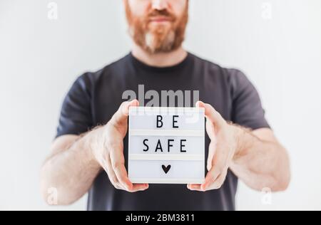 Concetto di salute e sicurezza. Uomo che tiene la scatola luminosa con il testo essere sicuro durante il coronavirus COVID-19 pandemics Foto Stock