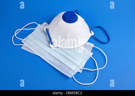 Maschere chirurgiche monouso per il viso e respiratore bianco su sfondo blu. Protezione contro la diffusione di infezioni. Respiratore per facciali filtranti n95 Foto Stock