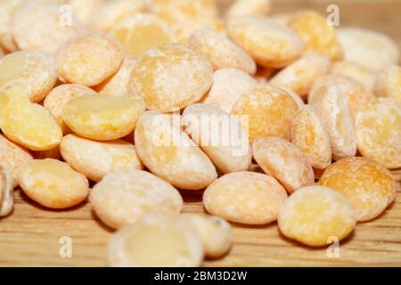 Piselli spezzati crudi di varietà gialla sulla superficie di legno e sparsi accanto, primo piano in selective focus. Cibo vegano, foto di scorta Foto Stock