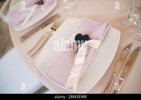 Ricevimento con tavolo per cena per matrimoni. Piatti bianchi quadrati su un tavolo rotondo con tovaglioli rosa con cuore nero. Sedie bianche Chiavari, Tiffany. Foto Stock