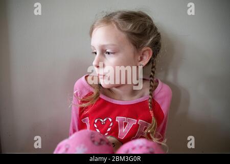 La ragazza bionda nelle trecce francesi in Pajamas sembra tristemente fuori-macchina fotografica Foto Stock