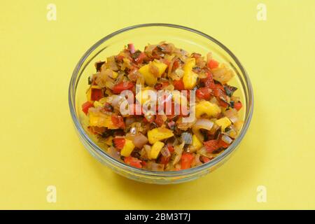 Salsa di mango cotta con peperoni rossi tritati e cipolla scalata in una ciotola di vetro su sfondo giallo Foto Stock