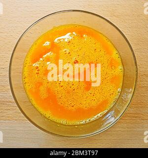 Miscela di colore arancione di uova di gallina in una ciotola di vetro trasparente sul tavolo da cucina, vista dall'alto, primo piano Foto Stock