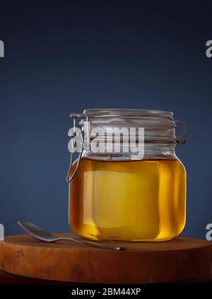 Vaso di miele con cucchiaio su tagliere di legno su sfondo blu Foto Stock