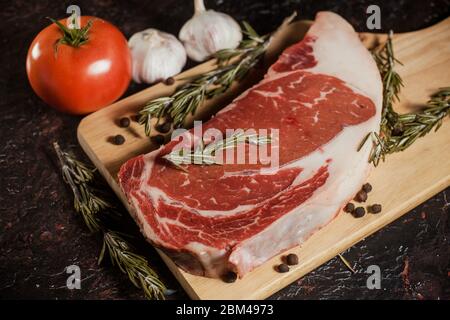 Bistecca di ribeye cruda con un rametto di rosmarino, aglio e pomodori Foto Stock