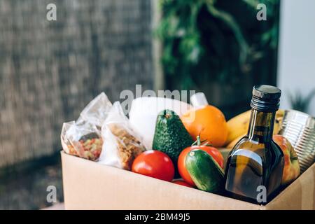 Scatola con cibo, carta igienica e igienizzatore per le mani sul tavolo in legno. Disposizione piatta. Focolaio di Covid-19, autoisolamento, consegna, concetto di donazione. Foto Stock