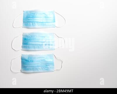 Fila di tre maschere facciali monouso di colore azzurro con fasce elastiche su sfondo bianco. Fotografato con una profondità di campo bassa con spazio di copia. Foto Stock