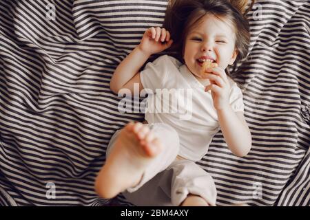 Ritratto di bella ragazza carina 3 anni sdraiata sul letto in abito e guardando la macchina fotografica Foto Stock