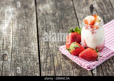 Yogurt bianco fruttato in vaso e fragole su tavolo di legno. Foto Stock