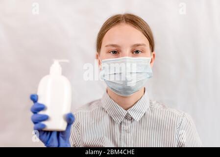 adolescente ragazza di 12-15 anni, in maschera medica protettiva copre il suo viso, in mano è bottiglia con sapone liquido, mani di lavaggio antisettico. Influenza Foto Stock