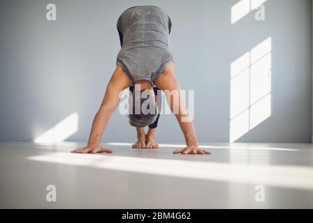 Basso angolo di maschio irriconoscibile bawooted in sportswear che mette a fuoco e facendo l'esercitazione di yoga del cane rivolta verso il basso mentre si allena da solo a casa Foto Stock