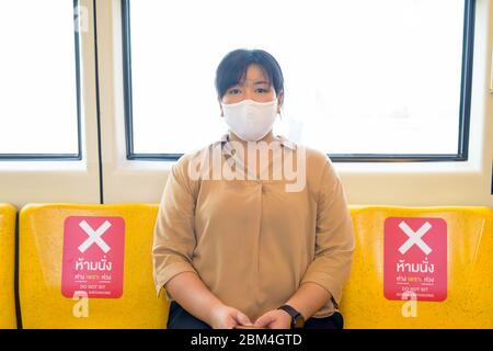 Donna asiatica sovrappeso con maschera seduta con distanza all'interno del treno Foto Stock