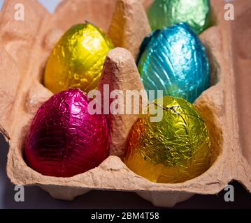 Uova di pasqua al cioccolato avvolte in un foglio colorato in un cartone di uova fresche Foto Stock