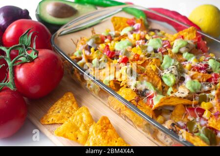 Piatto di nacho cotto in una teglia di vetro con scaglie di tortilla di mais, salsa Pico de gallo, avocado guacamole chipotle, fagioli, jalapenos e Monterrey jack c Foto Stock