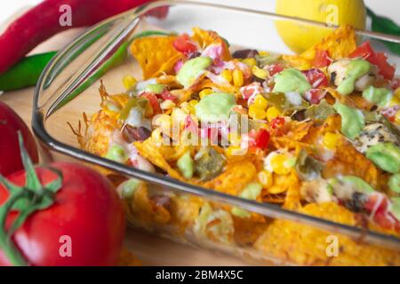 Piatto di nacho cotto in una teglia di vetro con scaglie di tortilla di mais, salsa Pico de gallo, avocado guacamole chipotle, fagioli, jalapenos e Monterrey jack c Foto Stock