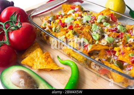 Piatto di nacho cotto in una teglia di vetro con scaglie di tortilla di mais, salsa Pico de gallo, avocado guacamole chipotle, fagioli, jalapenos e Monterrey jack c Foto Stock