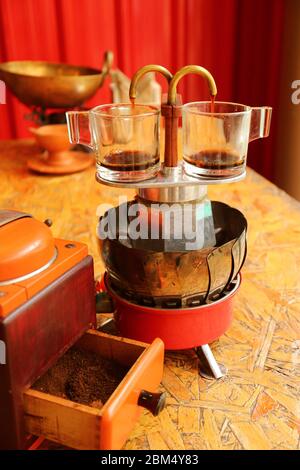 Due tazze di espresso in preparazione con una mini macchina per il caffè retro con macinacaffè in primo piano Foto Stock