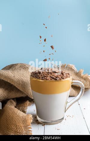 Caffè Dalgona su un tavolo di legno bianco. Polvere di cioccolato versata Foto Stock