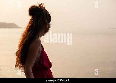 Donna siede sulla palma ammirando il tramonto su Chapora, Goa, India Foto Stock