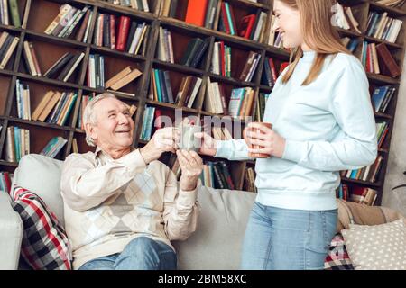 Padre e figlia a casa biblioteca donna che dà uomo tazza di caffè ridendo allegro Foto Stock