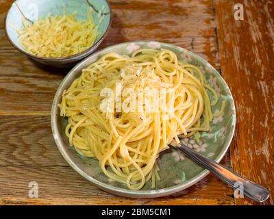 Porzioni Spaghetti Cacio e Pepe (pasta italiana con formaggio grattugiato e pepe macinato) e formaggio grattugiato in ciotole di ceramica giapponese su tavolo di legno vecchio in Foto Stock
