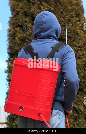 un giovane che porta un contenitore per un dispositivo speciale per spruzzare pesticidi su piante, lavorando in un giardino Foto Stock