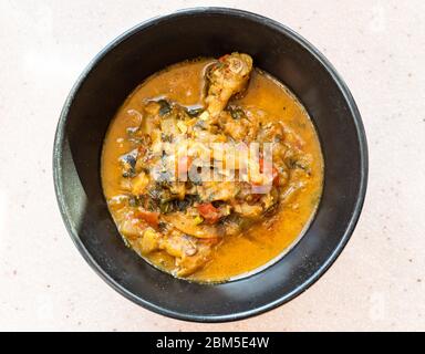 Vista dall'alto del Chakhokhbili (piatto georgiano tradizionale di pollo stufato, pomodoro, melanzane ed erbe fresche) in ciotola nera in cucina casalinga Foto Stock