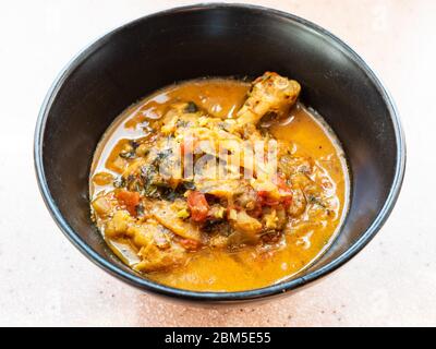 Chakhokhbili (piatto tradizionale georgiano di pollo stufato, pomodoro, melanzane ed erbe fresche) cucinato in una ciotola nera in cucina casalinga Foto Stock