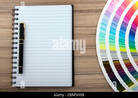 Gamma di carte colore su scrivania in legno con notebook e penna Foto Stock