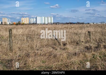 Vecchio campo rurale abbandonato con colonne rickety di recinzione di filo e nuovi edifici all'orizzonte Foto Stock