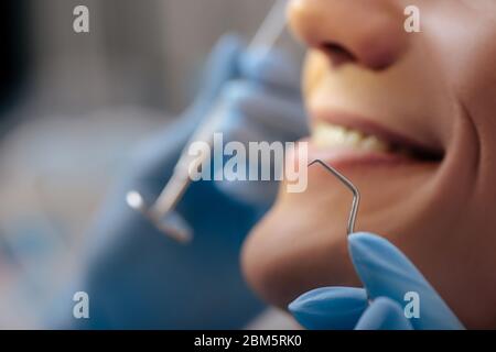 vista tagliata del dentista in guanti di lattice che tengono gli strumenti dentali vicino all'uomo allegro Foto Stock