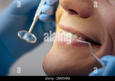 vista tagliata del dentista nei guanti in lattice che tengono gli strumenti dentali vicino all'uomo felice Foto Stock