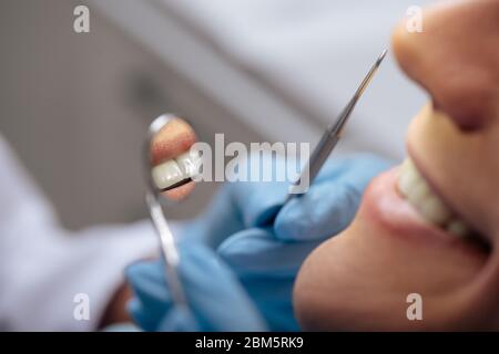 vista tagliata del dentista nei guanti in lattice che tengono gli strumenti dentali vicino all'uomo sorridente Foto Stock