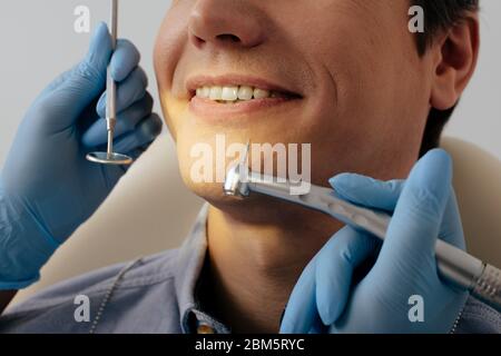 vista tagliata del dentista nei guanti in lattice che tengono gli strumenti dentali vicino a un paziente allegro Foto Stock