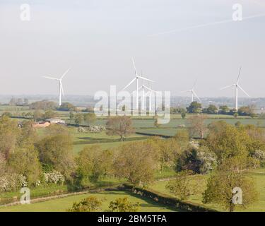 Northamptonshire, Regno Unito, 2020 maggio: Sei turbine eoliche si trovano in un mosaico di campi, circondate da siepi e alberi in campagna in una giornata primaverile. Foto Stock