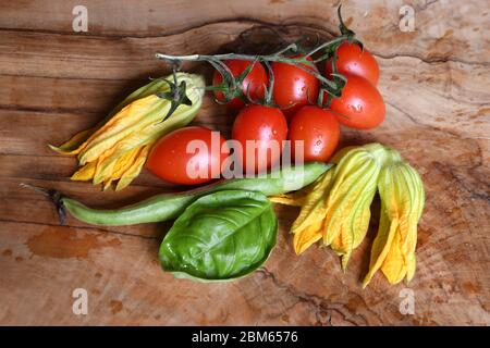 fiori di zucca gialli, foglie di basilico verde e pomodori rossi su tavola di legno Foto Stock