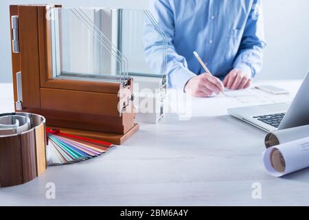 La sezione finestre con tripli vetri e telaio in legno e uomo al lavoro su un progetto di casa con il computer portatile su sfondo Foto Stock