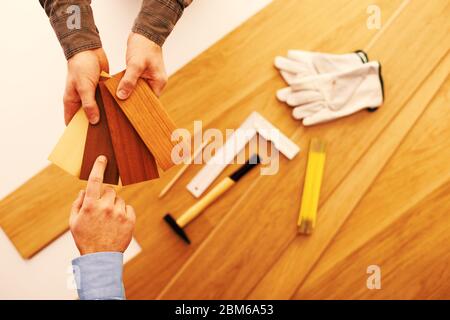 Falegname che mostra alcuni campioni di legno di baseboard ad un cliente e che sceglie un colore, installazione della pavimentazione e attrezzi di lavoro sullo sfondo Foto Stock