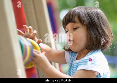 Cute bambina in età preschooler giocare all'aperto sul parco giochi in sole primavera day.Adorable piccolo bambino brunette impara a contare i numeri con cerchio di legno Foto Stock