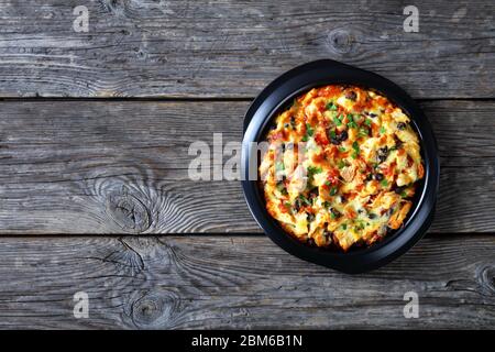 Torta di pollo caldo tamale di crosta di farina di mais con pollo tirato, formaggio cheddar, ripieno di fagioli neri cotto su un piatto di cottura nero cosparso di prezzemolo o Foto Stock