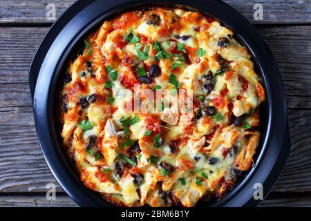 Torta di tamale sudamericana con crosta di mais con salsa di pomodoro, carne di pollo tirata, formaggio cheddar, ripieno di fagioli neri cotto su un piatto da forno nero, servire Foto Stock