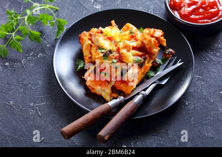 Cucina sudamericana pollo torta tamale o casseruola di pollo tirato con crosta di masa, formaggio cheddar, fagiolo nero servito su un piatto nero con posate Foto Stock