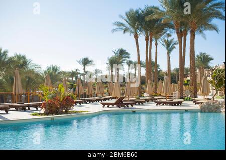 Estate chaise lounges sotto un ombrello sulla spiaggia di sabbia e le palme in hotel Egitto, Sharm el Sheikh, tempo di concetto per viaggiare senza persone Foto Stock