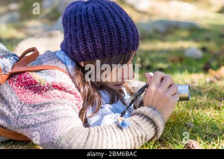 Donna con cappuccio di lana che giace sul terreno forestale mentre si utilizza una fotocamera per scattare una fotografia Foto Stock
